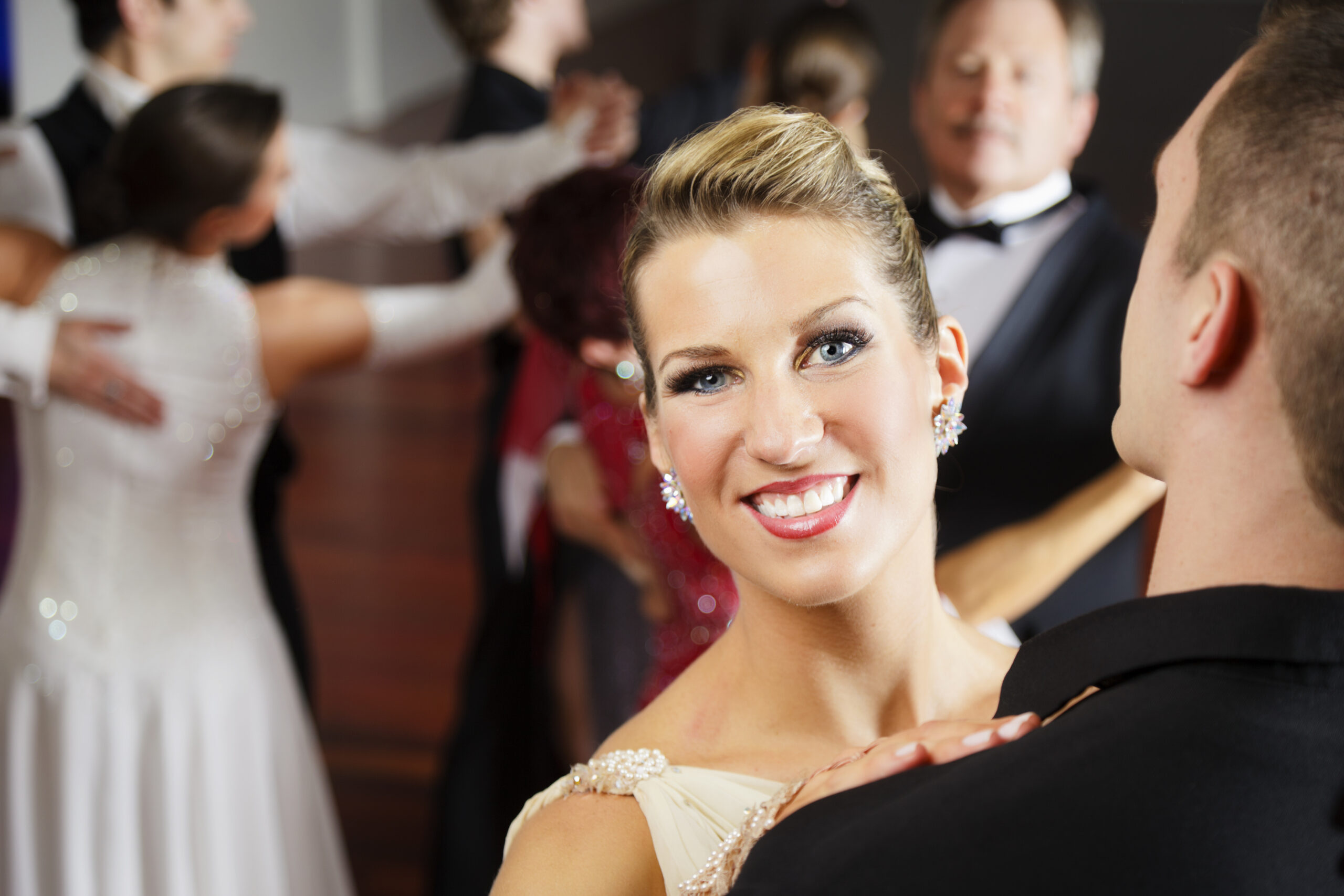 Smiling woman in a cream dress dancing with a partner at a formal ballroom event.