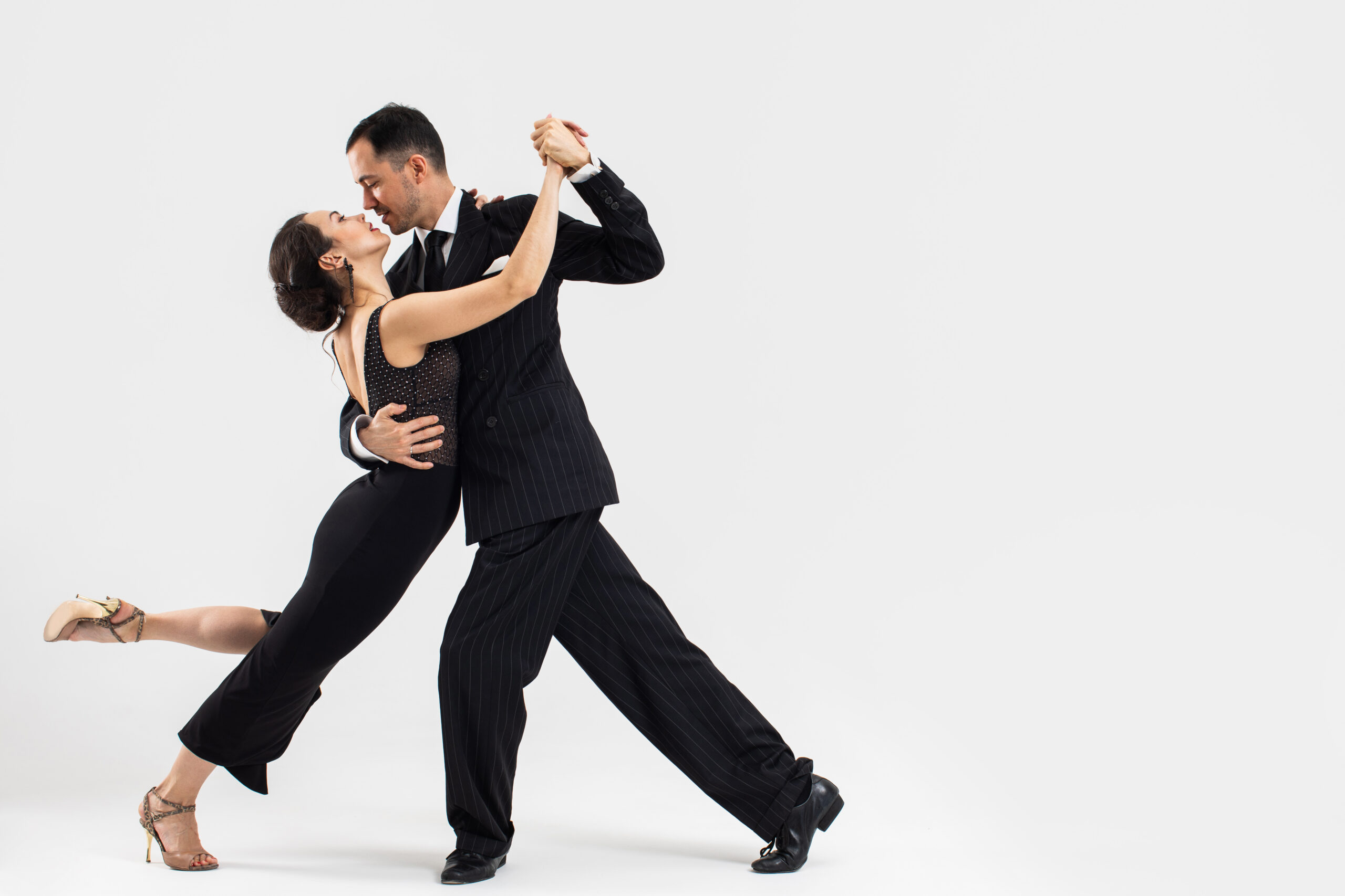 Pair of dancers performing a tango move in formal attire against a white studio backdrop.